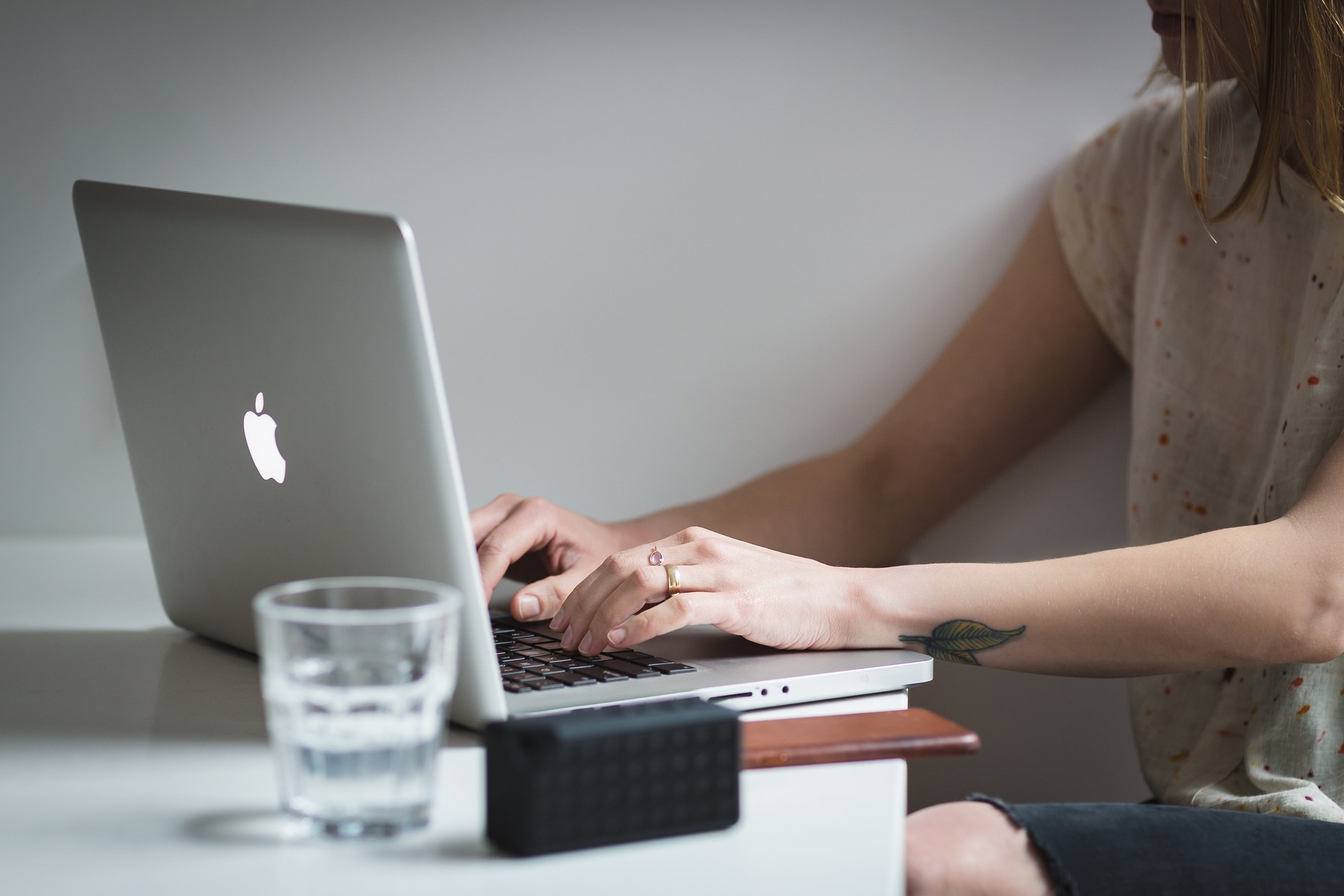 Persoon werkt op een laptop Persoon typt op een laptop aan een tafel, met een glas water en enkele boeken op de voorgrond.